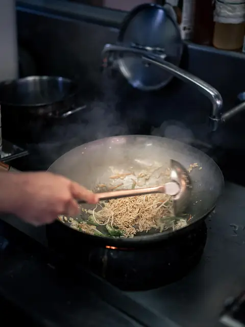 Des nouilles sautent dans un wok, sur le feu, en cuisine.