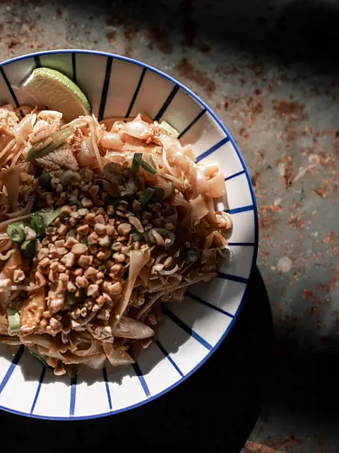Pad thaï aux cacahuètes et au citron vert, dans une assiette à rayures bleues.