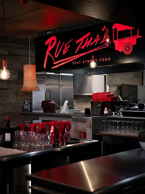 Le comptoir sous l'enseigne rouge lumineuse Rue Thaï, avec les verres alignés.