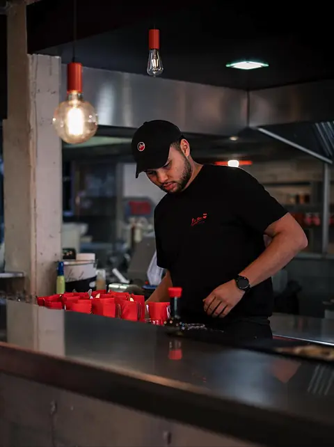 Un membre de l'équipe en casquette et T-shirt noir, au comptoir, sous une ampoule à filament.